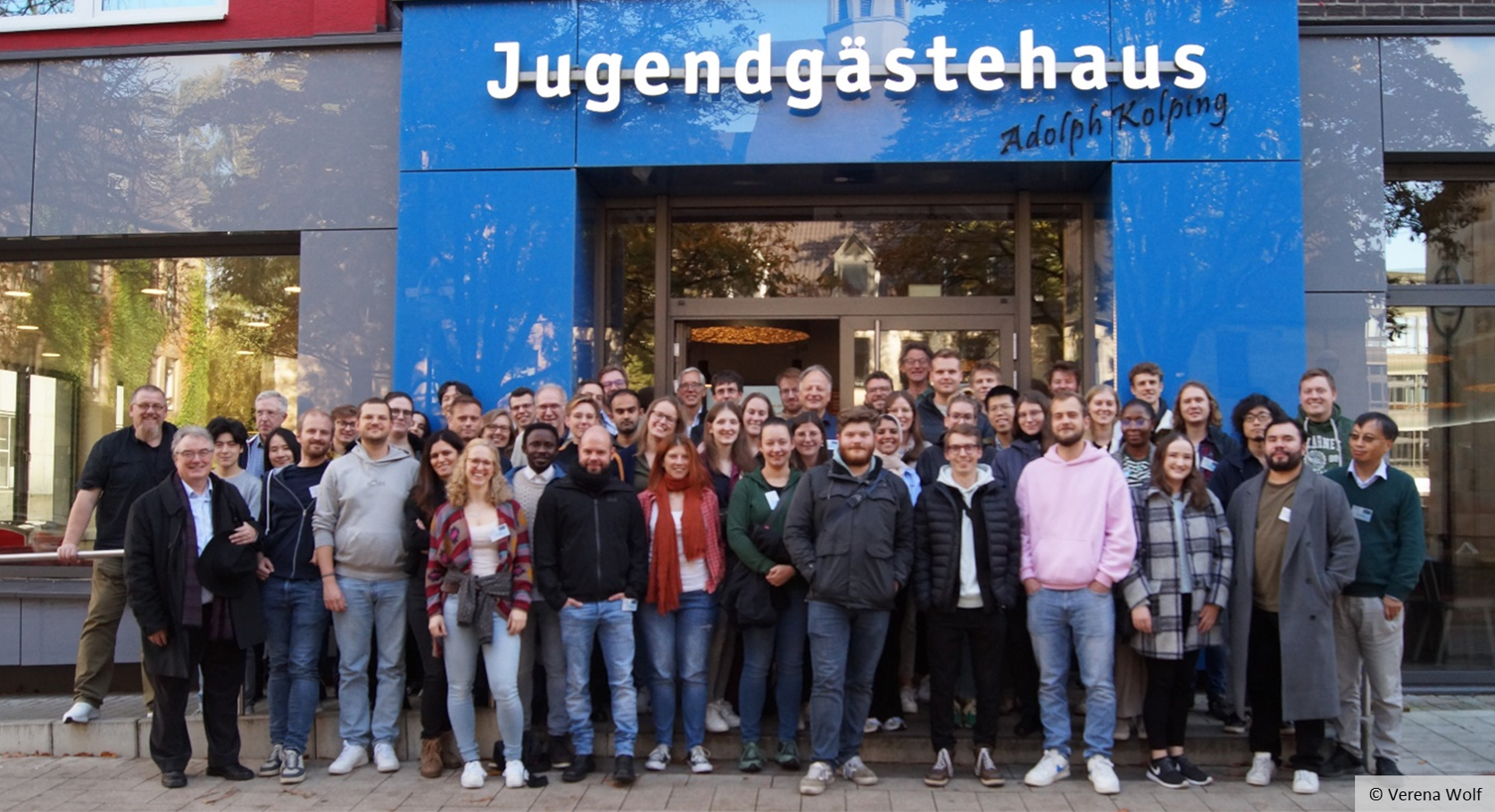 Eine große Personengruppe steht vor einem Gebäude. Über dem Gebäudeeingang ist der Schriftzug "Jugendgästehaus Adolph Kolping" zu lesen. Eine große Personengruppe steht vor einem Gebäude. Über dem Gebäudeeingang ist der Schriftzug "Jugendgästehaus Adolph Kolping" zu lesen.