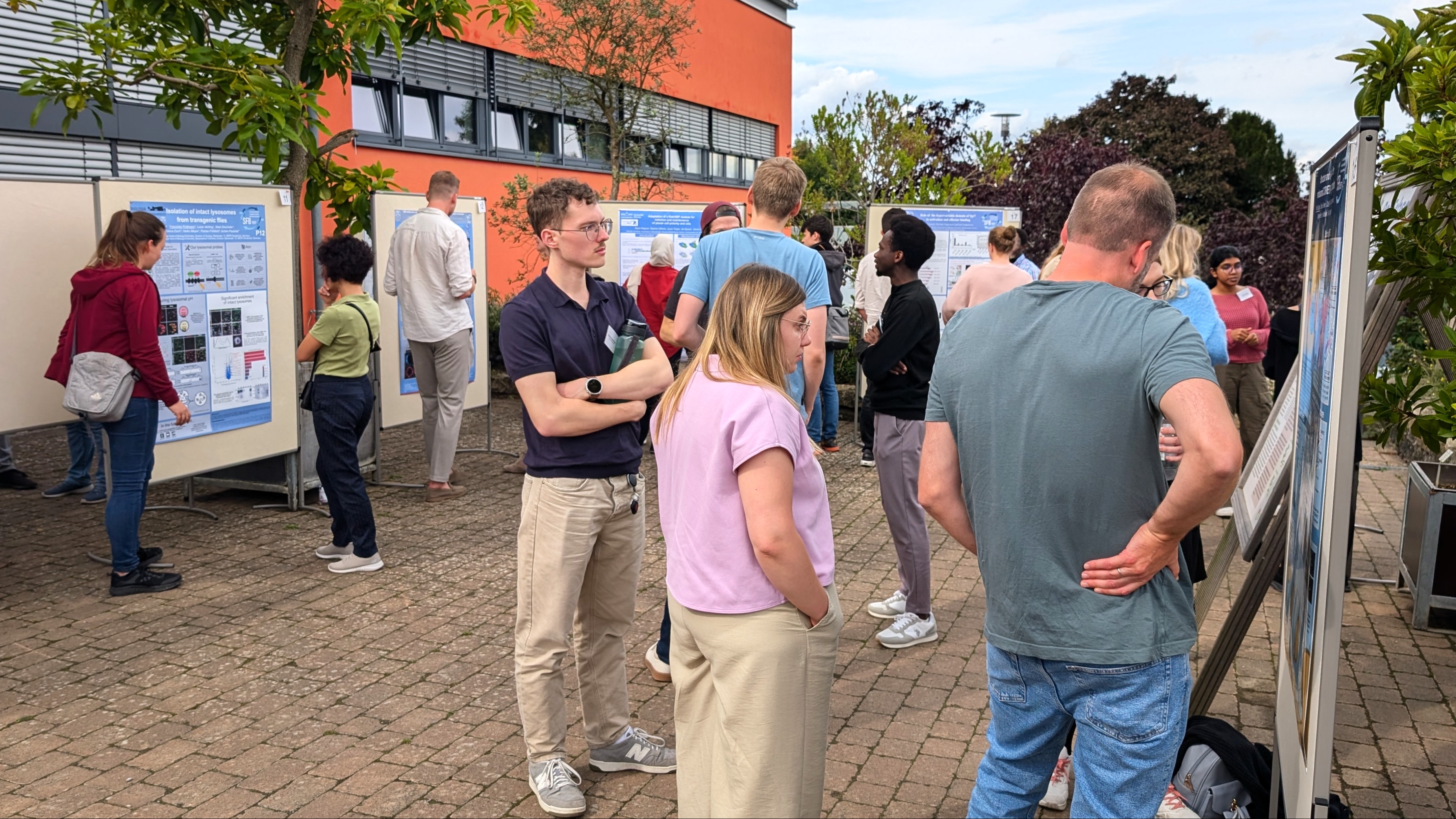 People are standing outdoors in front of poster boards displaying scientific posters.