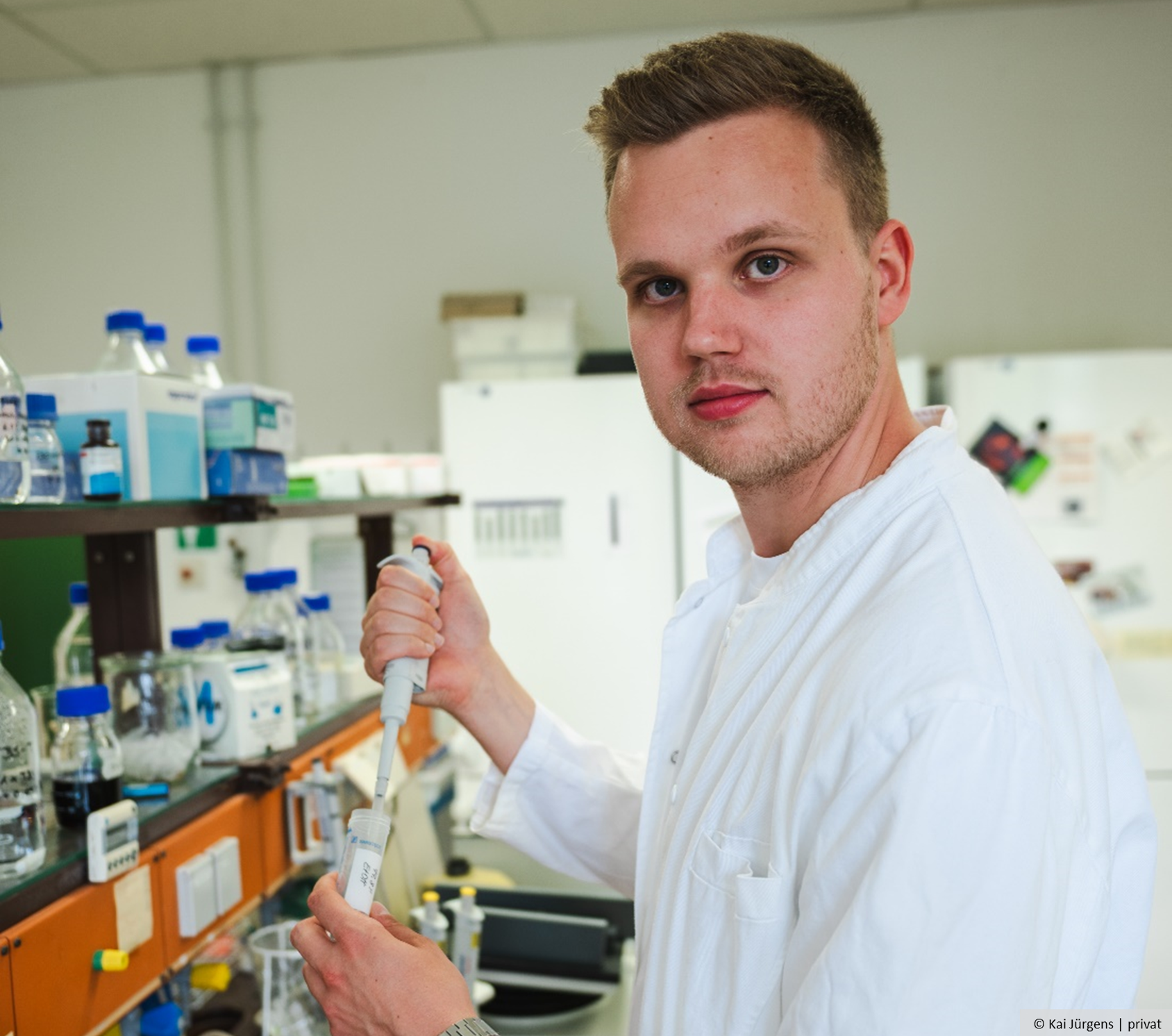 Ein Mann steht im Labor und hält eine Pipette in der Hand.